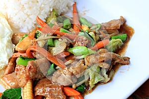 Delicious Thai dish chicken with stir fried vegetables in white dish with rice and fried egg on wooden table. Thai food.