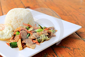 Delicious Thai dish chicken with stir fried vegetables in white dish with rice and fried egg on wooden table. Thai food.