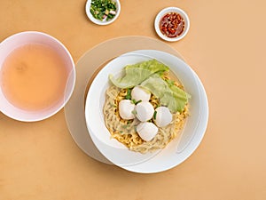 delicious thai food Fishball Noodle in bowl with soup, chili sauce and spring onion top view on wooden table