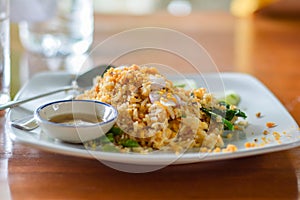 Delicious Thai food. Fried rice with egg, Kale served with minced red and green chilli in white plate on wooden table in cafe and