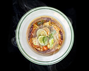Delicious Thai foods of Tom Yam Kung (Thai cuisine), Hot Thai food on the black background with smoke.Top view of Thai
