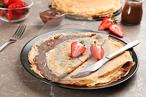 Delicious thin pancakes with chocolate paste and strawberries on grey marble table