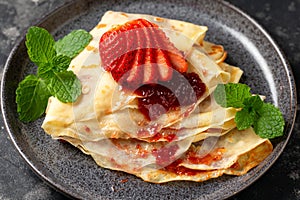 Delicious thin pancakes or crepes with strawberries and jam