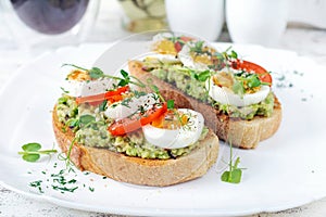 Delicious toast with avocado, boiled egg, tomatoes and microgreen on a white plate.