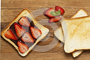 Delicious toast with fresh strawberries and chocolate paste on a wooden Board.