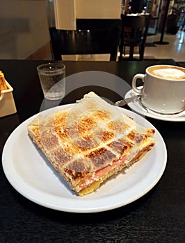 delicious toasted ham and cheese sandwich crumbs in triangles on white plate on a dark wooden table