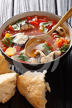 Delicious tomato fish soup with eel and vegetables close-up in a bowl served with bread. vertical