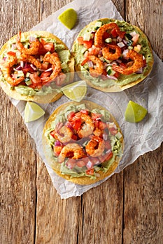 Delicious tostada with shrimps, fresh vegetables and guacamole close-up on a table. Vertical top view
