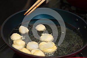 Brazilian homemade sweet called BOLINHO DE CHUVA being fried in a frying pan. Turning the dough with a chopstick photo