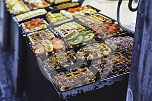 Delicious traditional LiÃ©ge waffles with colorful toppings on display in a store window in LiÃ©ge, Belgium