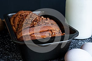 Delicious trenza bread garnished with ground nuts with a bottle of milk, eggs in front and a black background photo