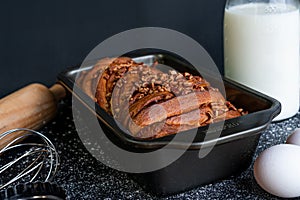 Delicious trenza bread garnished with ground nuts with a bottle of milk, eggs in front and a black background photo