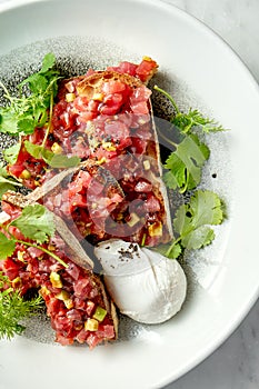 Delicious tuna tartare with avocado, cilantro, served on rye croutons in a white plate with poached egg. Snack of Japanese cuisine