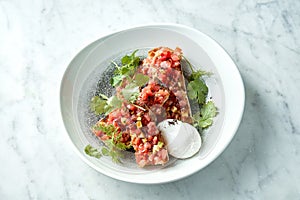 Delicious tuna tartare with avocado, cilantro, served on rye croutons in a white plate with poached egg. Snack of Japanese cuisine