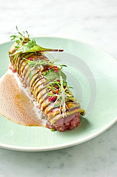 Delicious tuna tartare with avocado, cilantro, served on rye croutons in a white plate with poached egg. Snack of Japanese cuisine