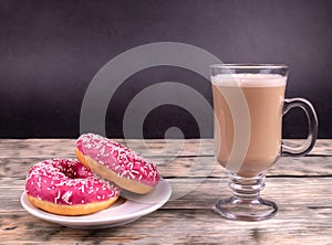 A delicious two pink donuts with white sprinkles and a cup of coffee with milk