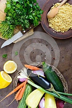 Delicious useful porridge cous cous in a clay plate and raw fresh vegetables in a basket, greens, lemon.