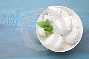 Delicious vanilla ice cream and mint in bowl on light blue wooden table, top view. Space for text