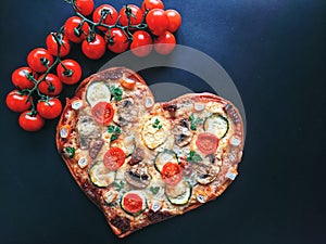 Delicious vegetarian heart shaped pizza with tomatoes, vegetables and cheese for Valentine`s Day on black background.