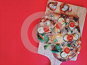 Delicious vegetarian heart shaped pizza with tomatoes, vegetables and cheese for Valentine`s Day on red background.