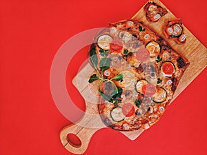 Delicious vegetarian heart shaped pizza with tomatoes, vegetables and cheese for Valentine`s Day on red background.