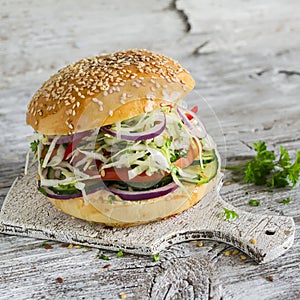 Delicious veggie burger with cabbage, tomato, cucumber, onions and peppers on a light wooden surface