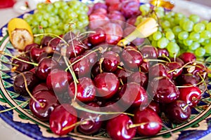 Delicious vibrant colored fresh fruits and berries variety on an asian patterned plate: sweet cherries, bananas, graped