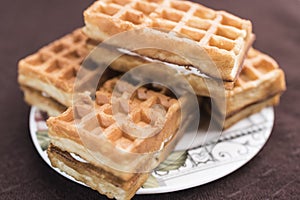 Delicious Viennese waffles with a filling lie on a saucer on a dark brown background