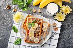 Delicious waffles with banana slices and glass of milk on grey table