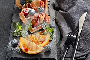 Delicious waffles heart shape with caramelized banana and berries on serving board on grey background. Dessert. Serving food