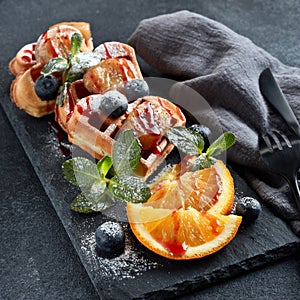 Delicious waffles heart shape with caramelized banana and berries on serving board on grey background. Dessert. Serving food