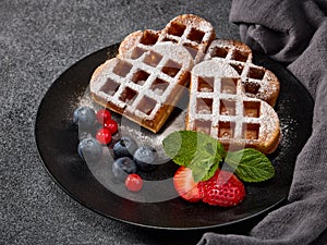 Delicious waffles heart shape with  powdered sugar and berries on  plate on grey background. Sweet meal. Dessert