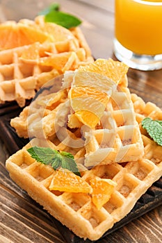 Delicious waffles with orange slices on wooden board