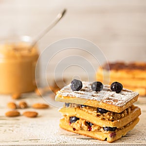 Delicious waffles with peanut paste and blueberries, on a light background
