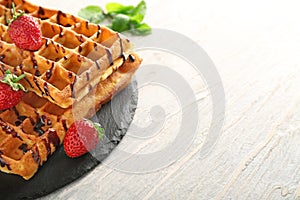 Delicious waffles with strawberries and chocolate sauce on wooden table