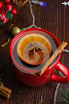 Delicious warm mulled wine with cinnamon, star anise and orange in a red cup on christmas background, vertical frame