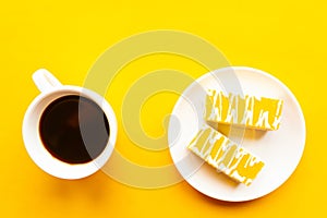 Delicious yellow cakes on a plate and coffee cup, top view. Bright yellow background