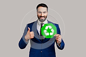 Delighted bearded businessman holding pointing at green recycling sign, saving environment.
