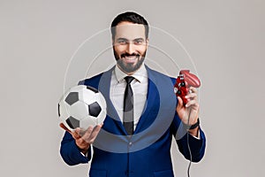 Delighted bearded man holding joypad and soccer black and white classic ball, football video game.