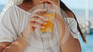 Delighted brunette woman enjoys her orange juice at sea beach cafe. Essence of summertime, holiday escape, relaxation