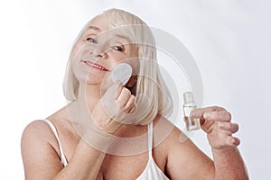 Delighted elderly woman having her daily skin care routine