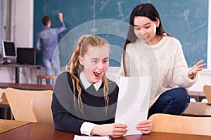 Delighted schoolgirl and Chinese girl schoolmate reading notification photo