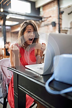 Delighted  female watching content on her laptop with headphones in ears and fists up in YES position