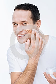 Delighted happy man applying moisturizing cream