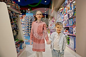 Delighted little children walk among display cases with toys in store