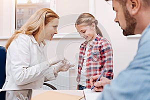 Delighted little female patient looking at hands of pediatrician