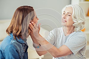 Delighted loving senior woman holding cheeks of her daughter