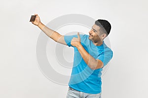 Delighted man blogger with mobile phone, has video call or livestream showing thumb up, like gesture