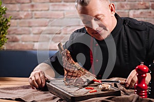 Delighted man chopping steak with vegetables