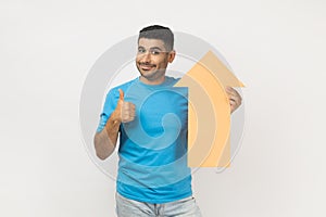 Delighted man holding carton arrow indicating up, being glad of career success, showing thumb up.